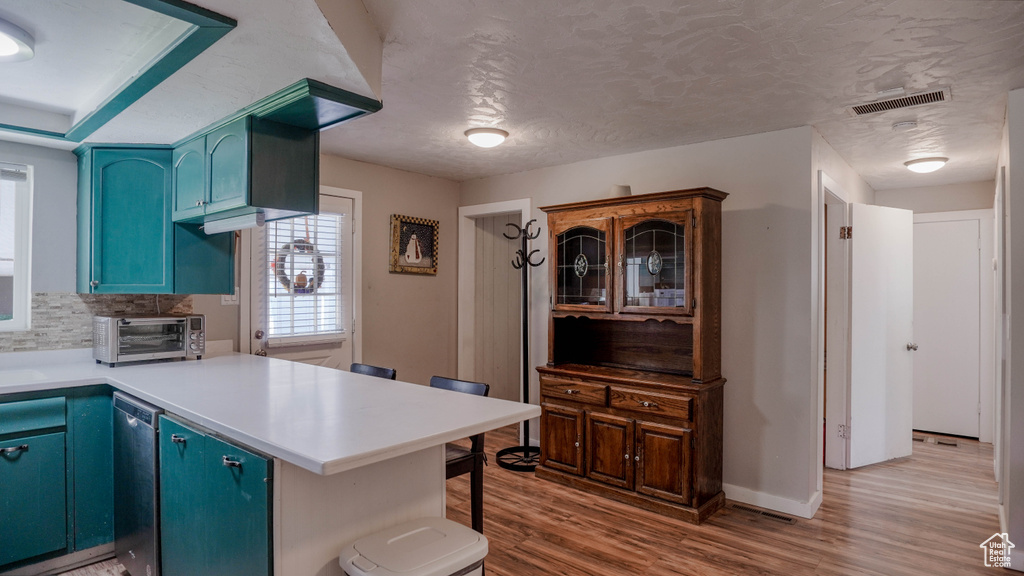 Kitchen featuring light hardwood / wood-style floors, kitchen peninsula, dishwasher, and blue cabinetry