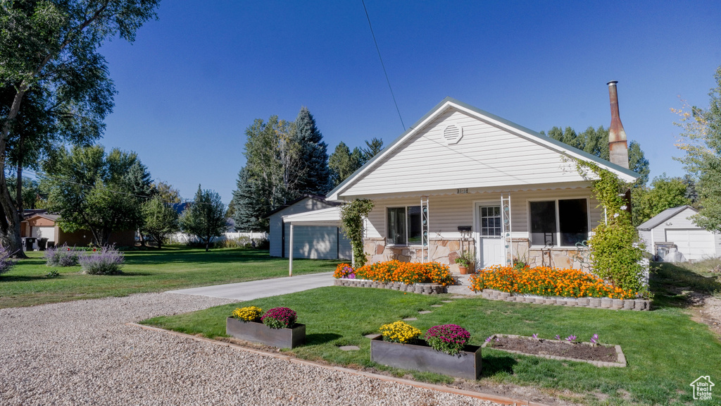 View of front facade featuring a front yard, covered porch, an outdoor structure, and a garage