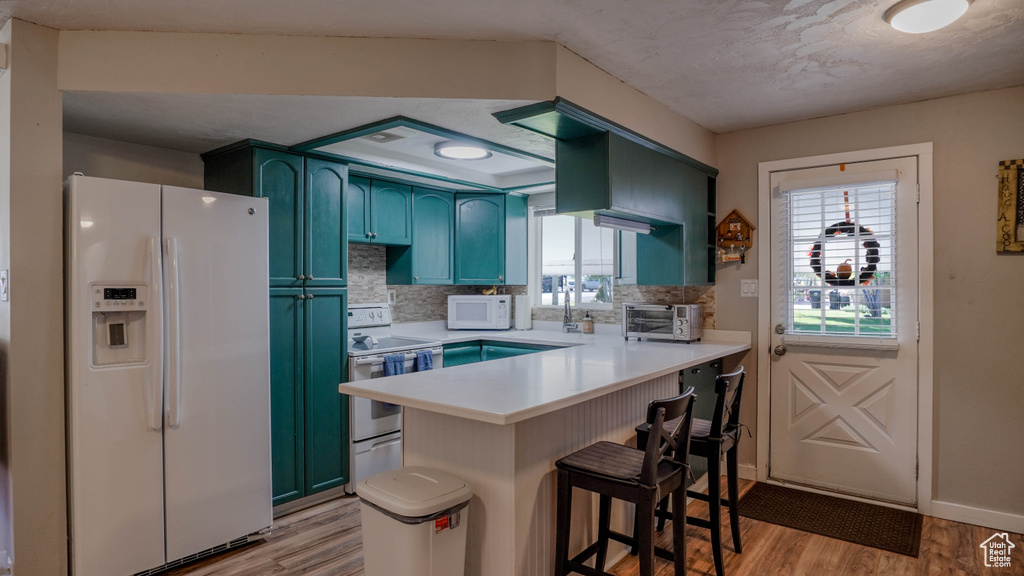 Kitchen with light wood-type flooring, a breakfast bar area, kitchen peninsula, white appliances, and backsplash