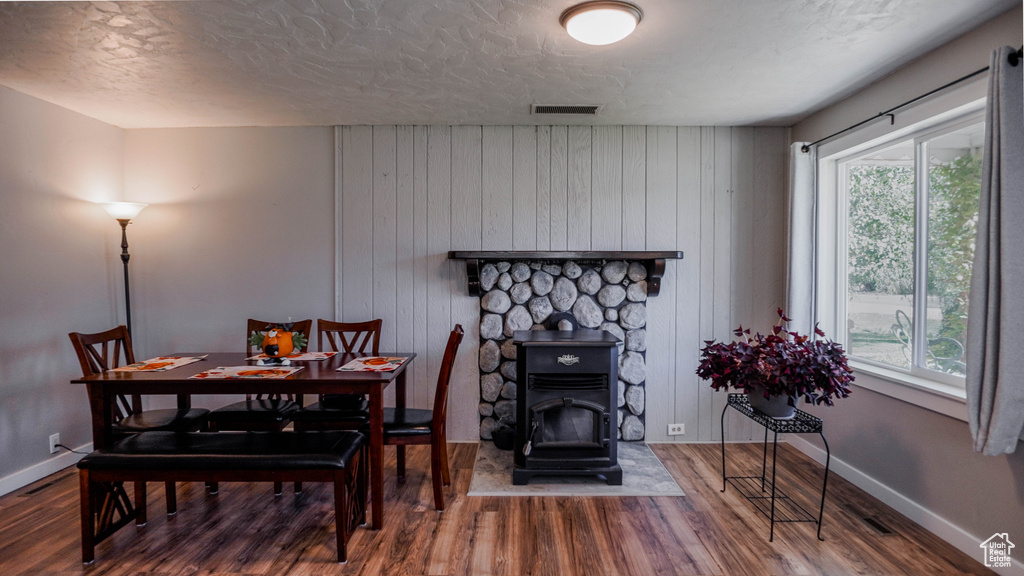 Dining room featuring a fireplace, wood walls, a wood stove, a textured ceiling, and hardwood / wood-style floors