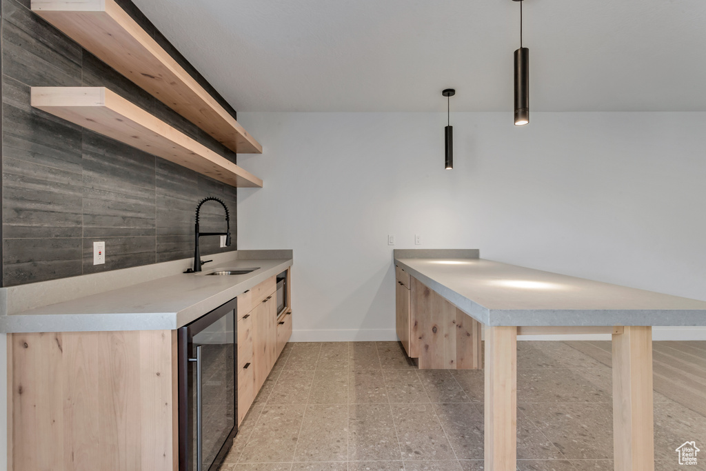 Kitchen with wine cooler, backsplash, light brown cabinets, decorative light fixtures, and sink