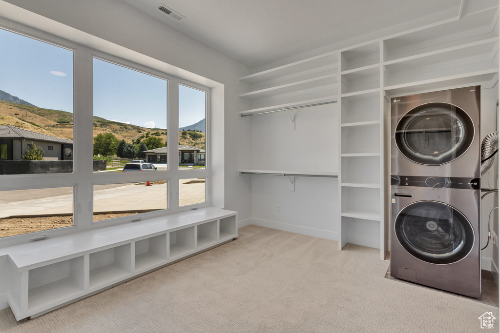 Laundry area featuring light colored carpet, stacked washer and dryer, and a mountain view