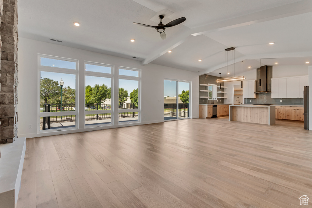 Unfurnished living room featuring lofted ceiling with beams, sink, ceiling fan, and light hardwood / wood-style flooring