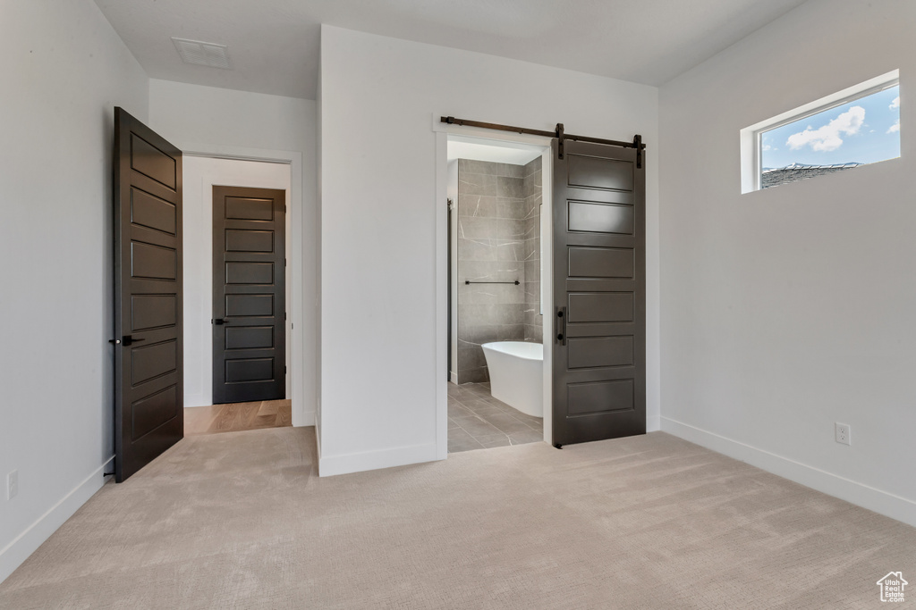 Unfurnished bedroom with connected bathroom, light colored carpet, and a barn door