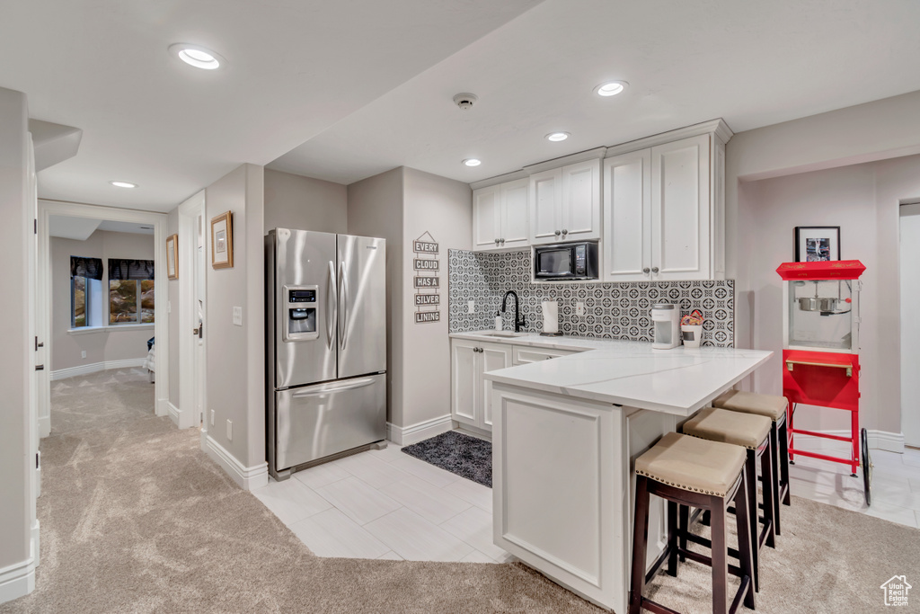 Kitchen with a kitchen breakfast bar, white cabinets, backsplash, stainless steel fridge with ice dispenser, and light colored carpet