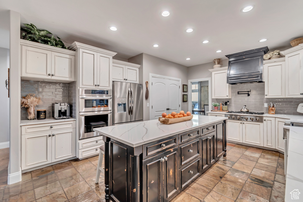 Kitchen with white cabinetry, appliances with stainless steel finishes, a kitchen island, and custom exhaust hood