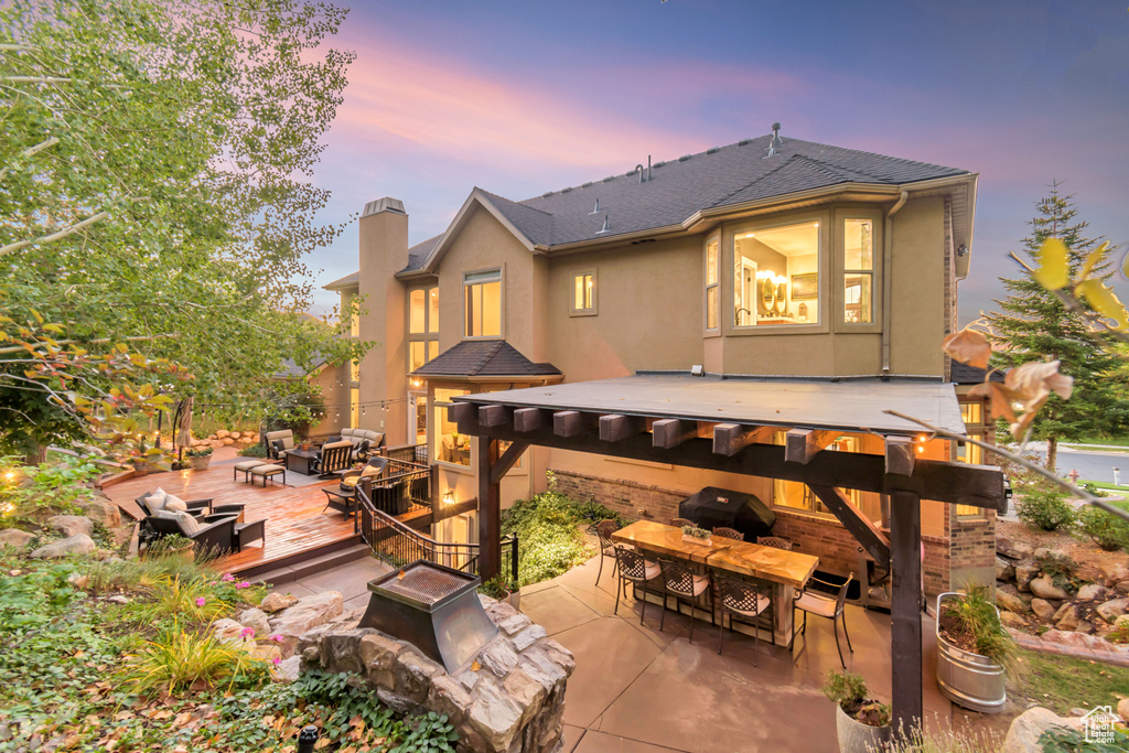 Back house at dusk featuring a pergola, a patio, a bar, and a deck