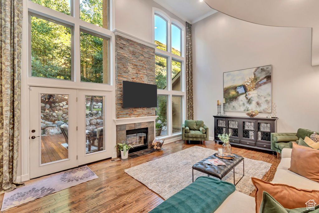 Living room featuring light hardwood / wood-style flooring, a towering ceiling, ornamental molding, and a tiled fireplace