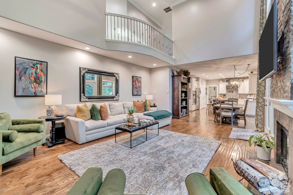 Living room with an inviting chandelier, a high ceiling, a tiled fireplace, and light hardwood / wood-style flooring