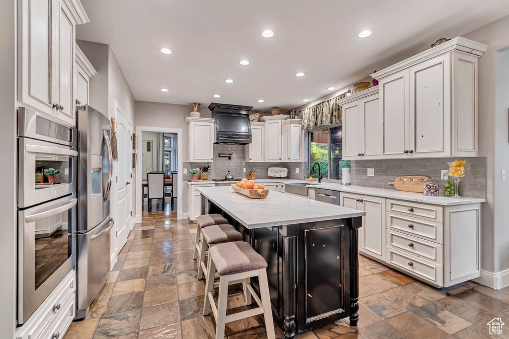 Kitchen with custom range hood, white cabinets, a breakfast bar, a kitchen island, and stainless steel appliances