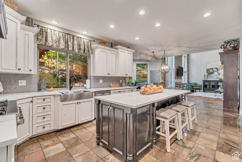 Kitchen with decorative backsplash, white cabinetry, a center island, decorative light fixtures, and sink