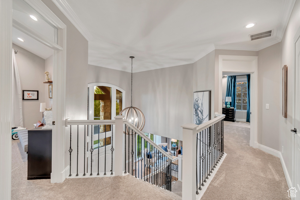 Corridor with light colored carpet, an inviting chandelier, and crown molding