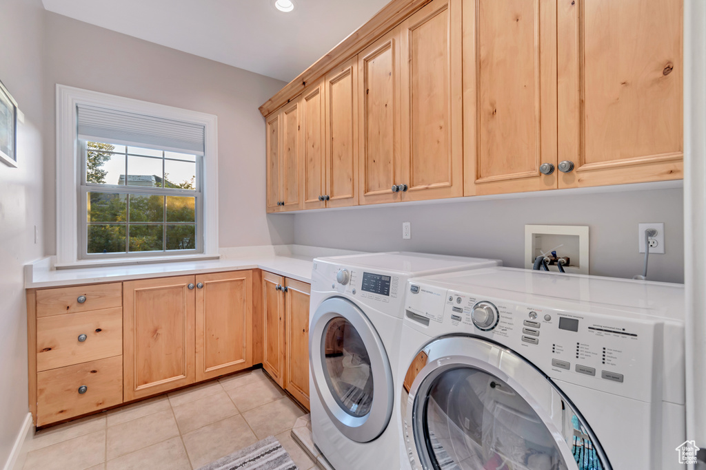 Laundry area featuring light tile patterned flooring, washer and dryer, and cabinets