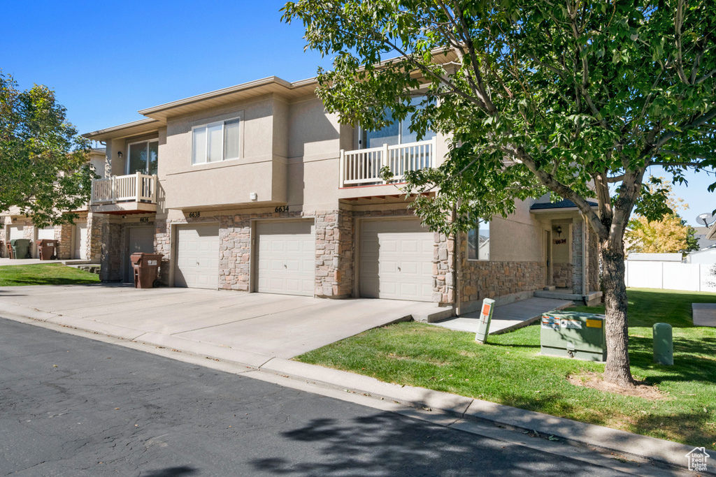 Townhome / multi-family property with a balcony, a front lawn, and a garage