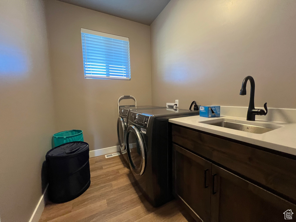 Clothes washing area featuring light wood-type flooring, sink, independent washer and dryer, and cabinets