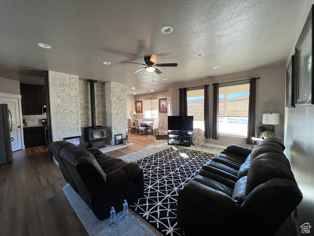 Living room with a textured ceiling, ceiling fan, a wood stove, and hardwood / wood-style flooring