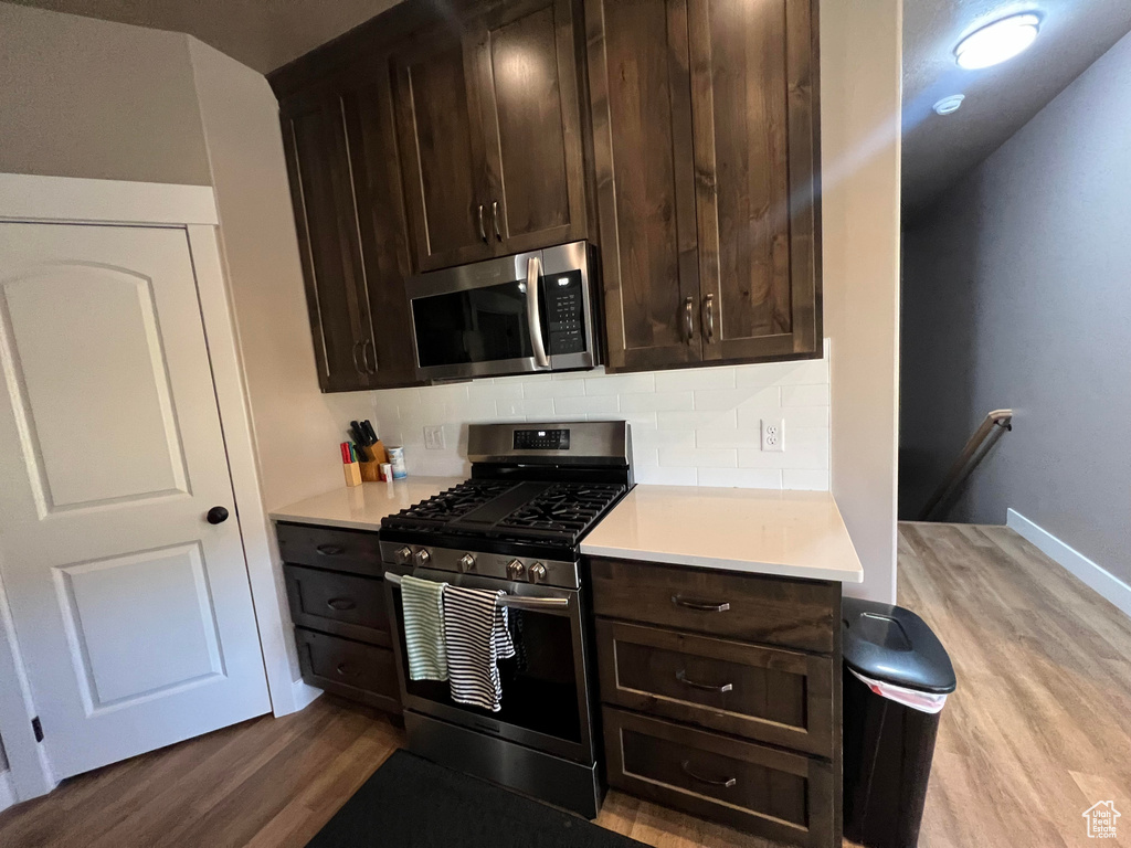 Kitchen with dark brown cabinets, light hardwood / wood-style flooring, stainless steel appliances, and tasteful backsplash