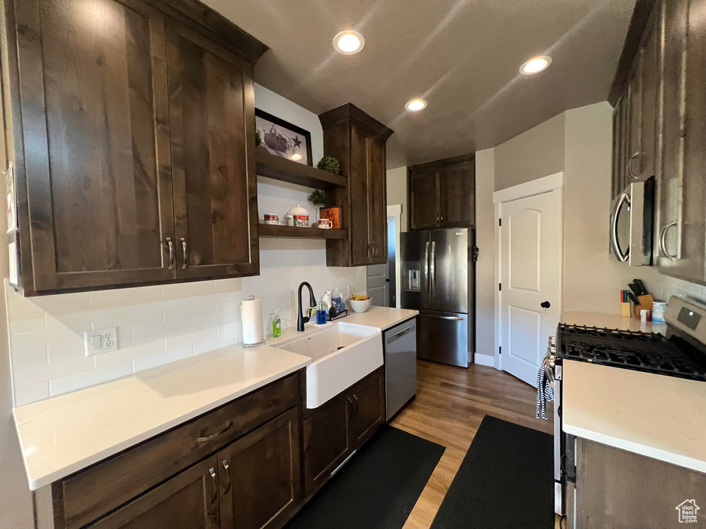 Kitchen featuring appliances with stainless steel finishes, light hardwood / wood-style floors, backsplash, dark brown cabinetry, and sink