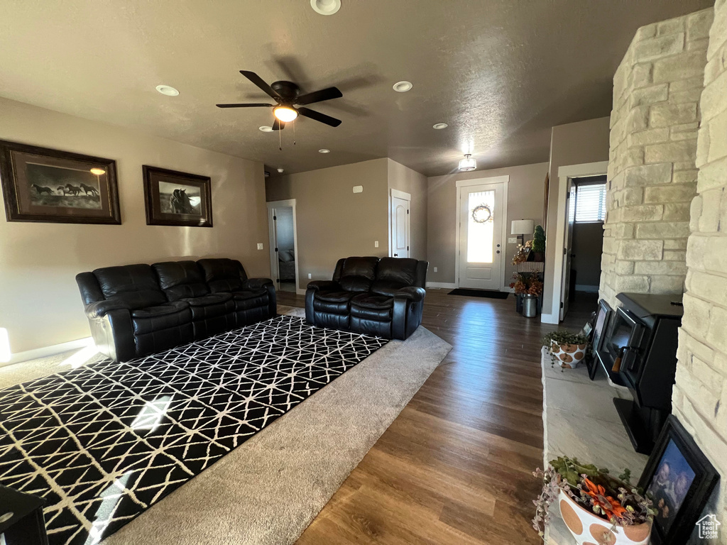 Living room with ceiling fan, a stone fireplace, a textured ceiling, and wood-type flooring