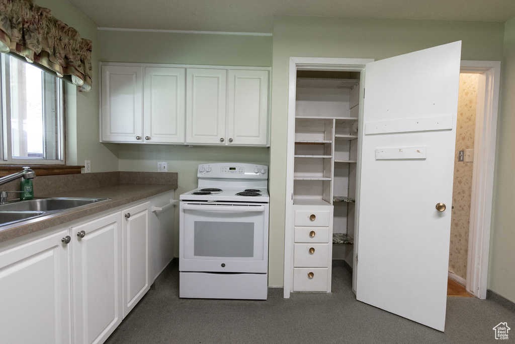 Kitchen featuring white electric stove, dark colored carpet, sink, and white cabinets