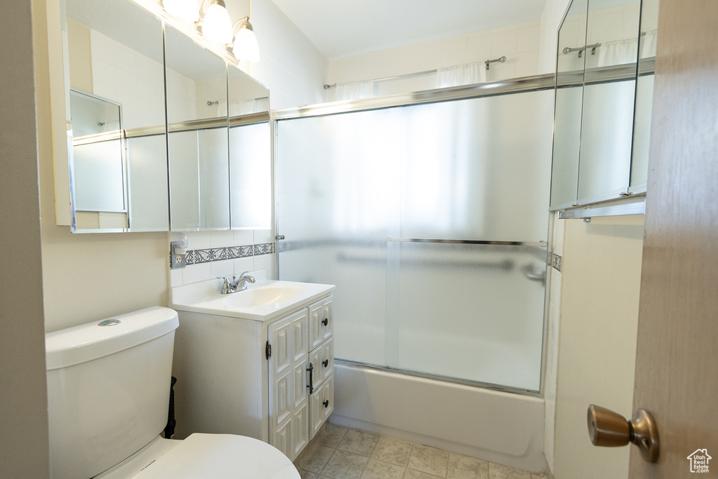 Full bathroom featuring bath / shower combo with glass door, vanity, toilet, and tasteful backsplash