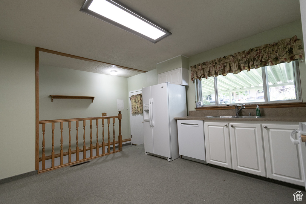 Kitchen with white appliances, white cabinetry, sink, and light carpet