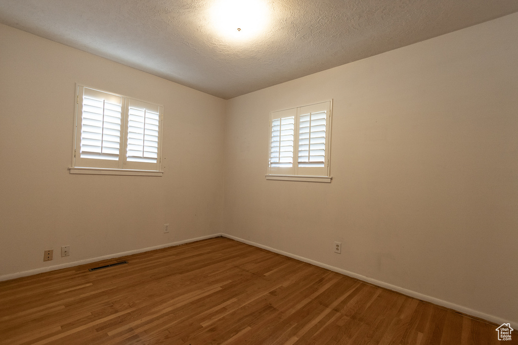 Spare room featuring a textured ceiling, hardwood / wood-style flooring, and a healthy amount of sunlight