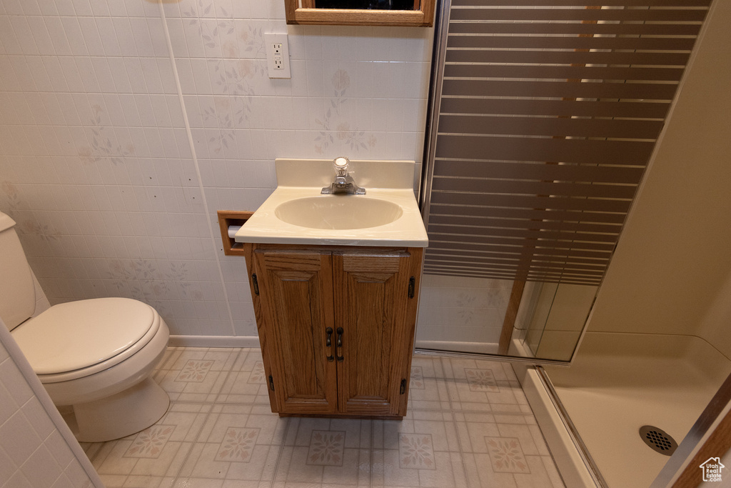 Bathroom with tile walls, a shower with shower door, vanity, and toilet