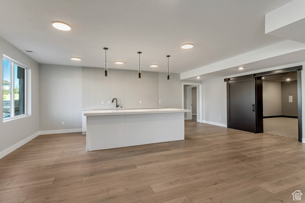 Kitchen with an island with sink, light hardwood / wood-style floors, decorative light fixtures, and sink