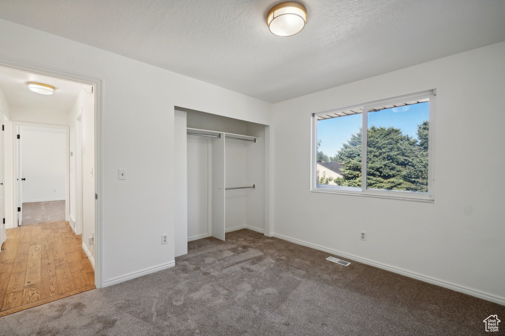 Unfurnished bedroom with light colored carpet, a textured ceiling, and a closet