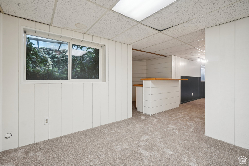 Basement featuring wood walls, a drop ceiling, and carpet flooring