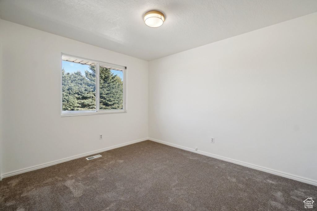 Empty room with a textured ceiling and dark colored carpet