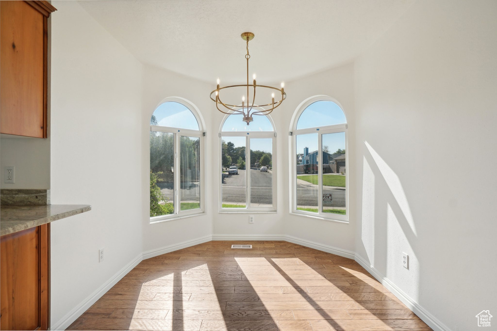 Unfurnished dining area with light hardwood / wood-style floors, vaulted ceiling, and a notable chandelier