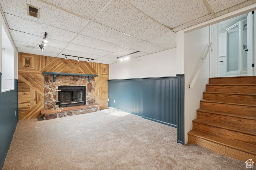 Basement with a fireplace, carpet flooring, a drop ceiling, track lighting, and wooden walls