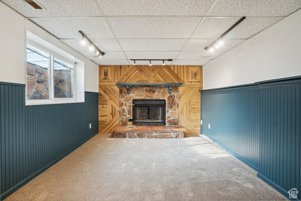 Unfurnished living room with wood walls, track lighting, carpet flooring, and a stone fireplace