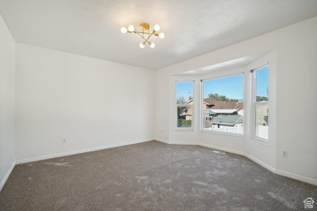 Carpeted spare room featuring a chandelier