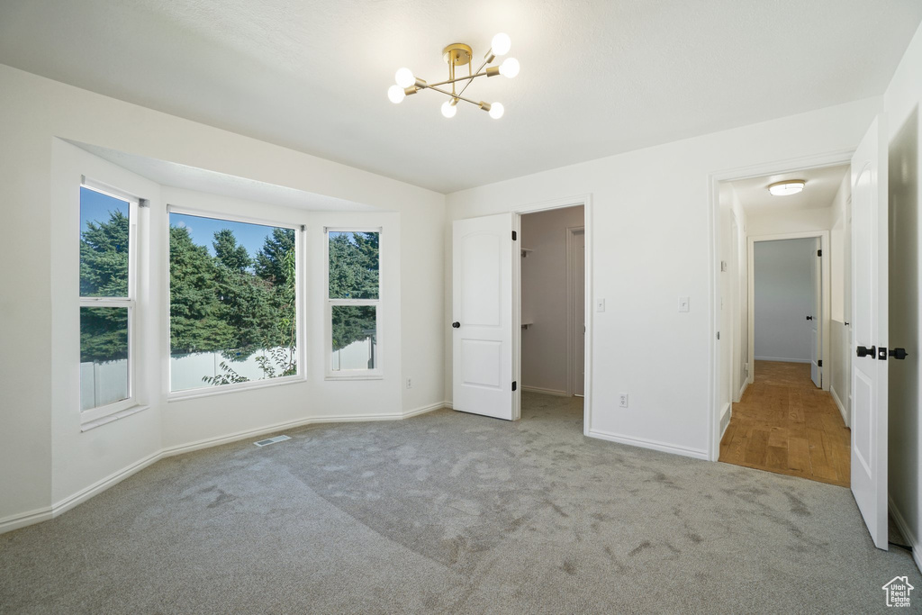 Unfurnished bedroom with a notable chandelier and light colored carpet