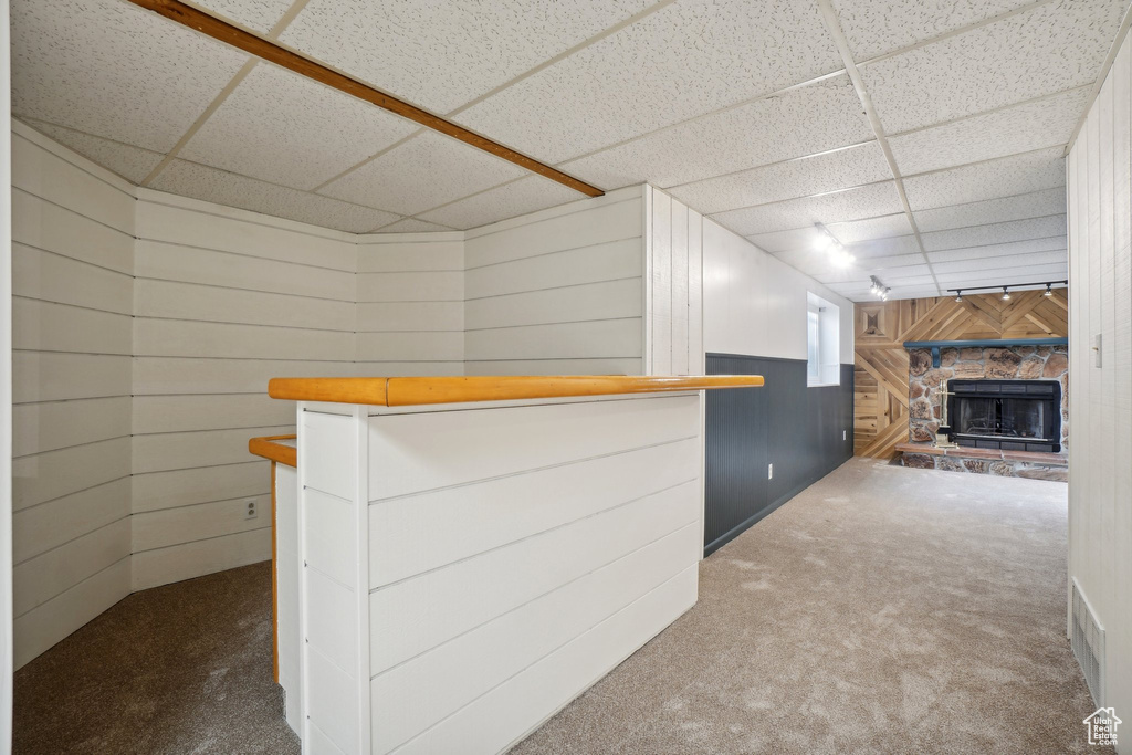 Bar featuring carpet, a drop ceiling, wooden walls, and a fireplace