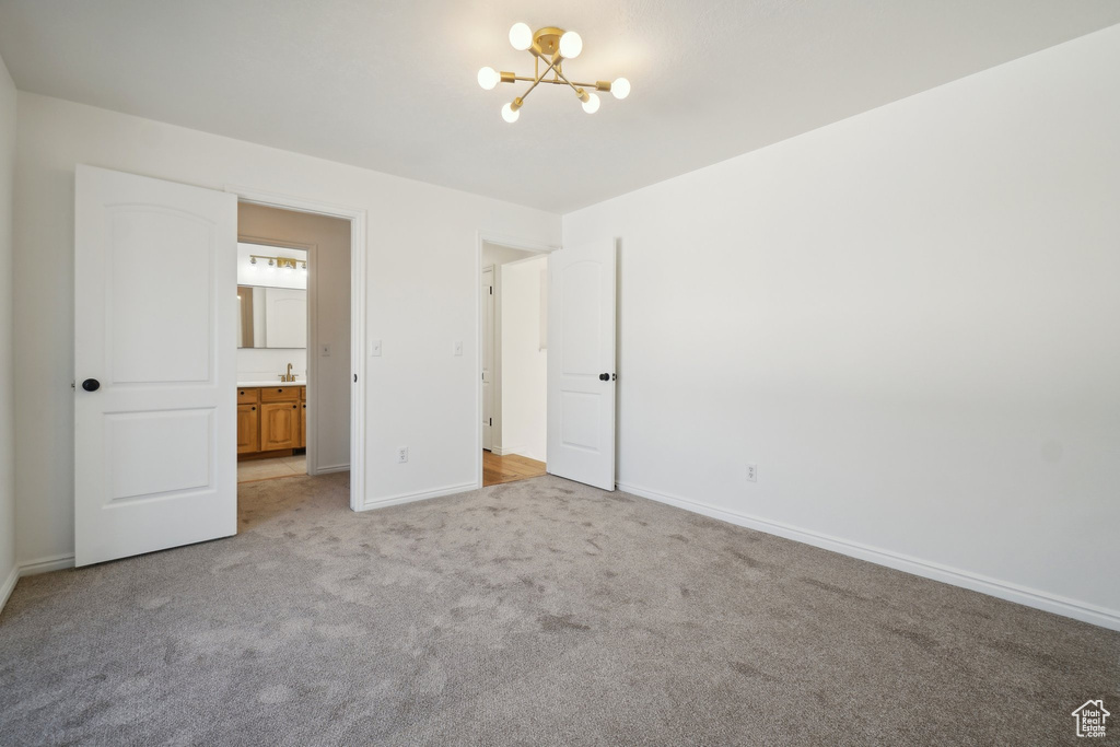 Unfurnished bedroom featuring light carpet, ensuite bath, and a chandelier