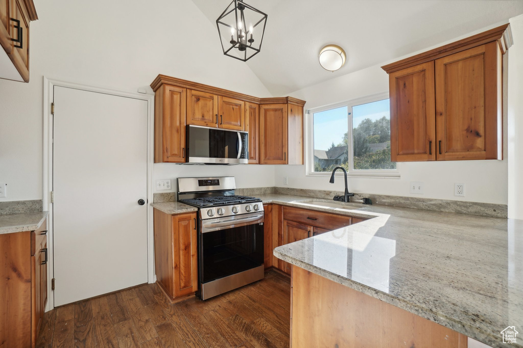 Kitchen with vaulted ceiling, kitchen peninsula, an inviting chandelier, appliances with stainless steel finishes, and decorative light fixtures