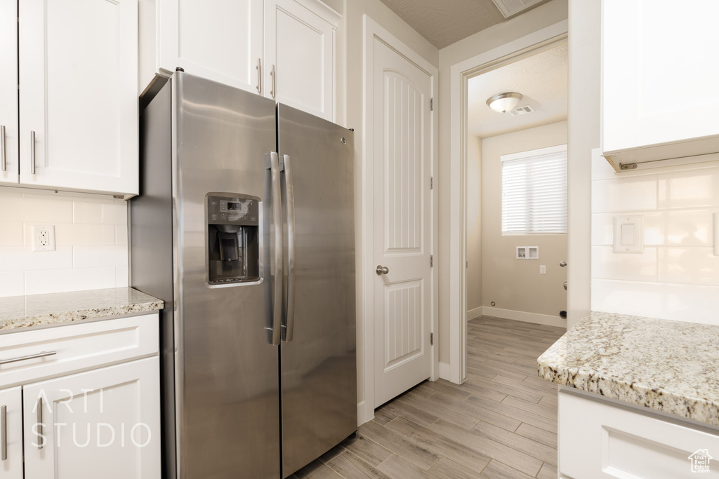 Kitchen featuring stainless steel refrigerator with ice dispenser, light hardwood / wood-style floors, light stone countertops, and white cabinets