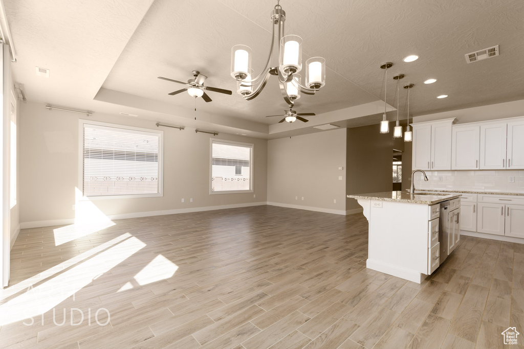 Kitchen with ceiling fan with notable chandelier, white cabinetry, light hardwood / wood-style floors, and an island with sink