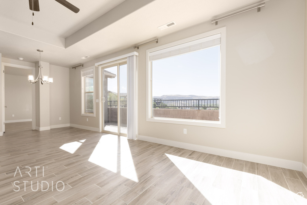 Empty room with light wood-type flooring and ceiling fan with notable chandelier