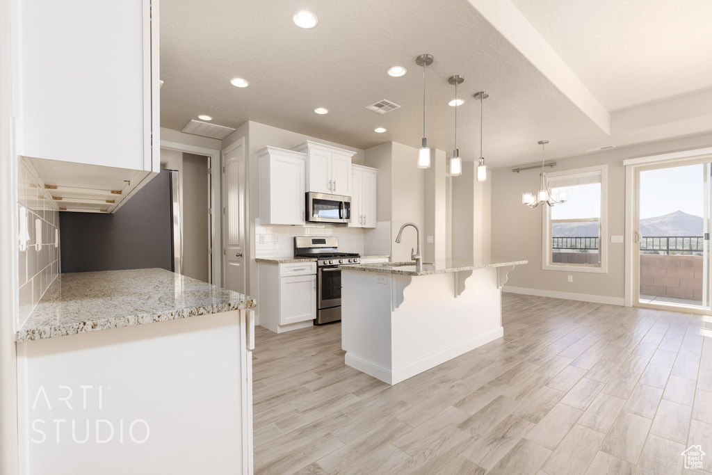 Kitchen featuring appliances with stainless steel finishes, light hardwood / wood-style floors, white cabinetry, a breakfast bar area, and pendant lighting