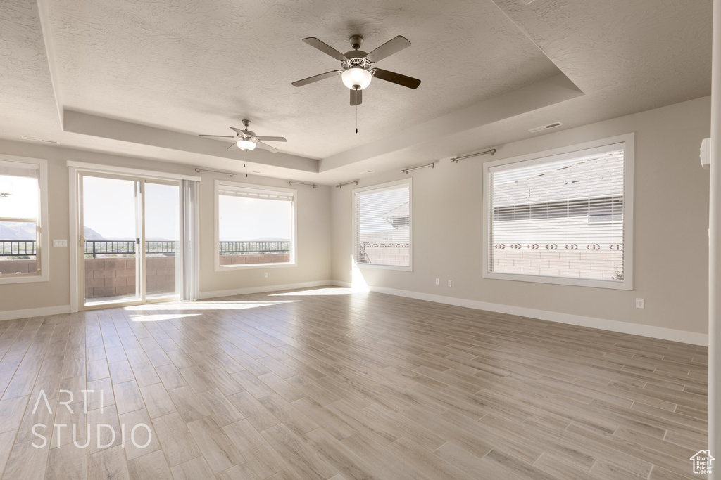 Empty room with a textured ceiling, light hardwood / wood-style floors, a tray ceiling, and ceiling fan