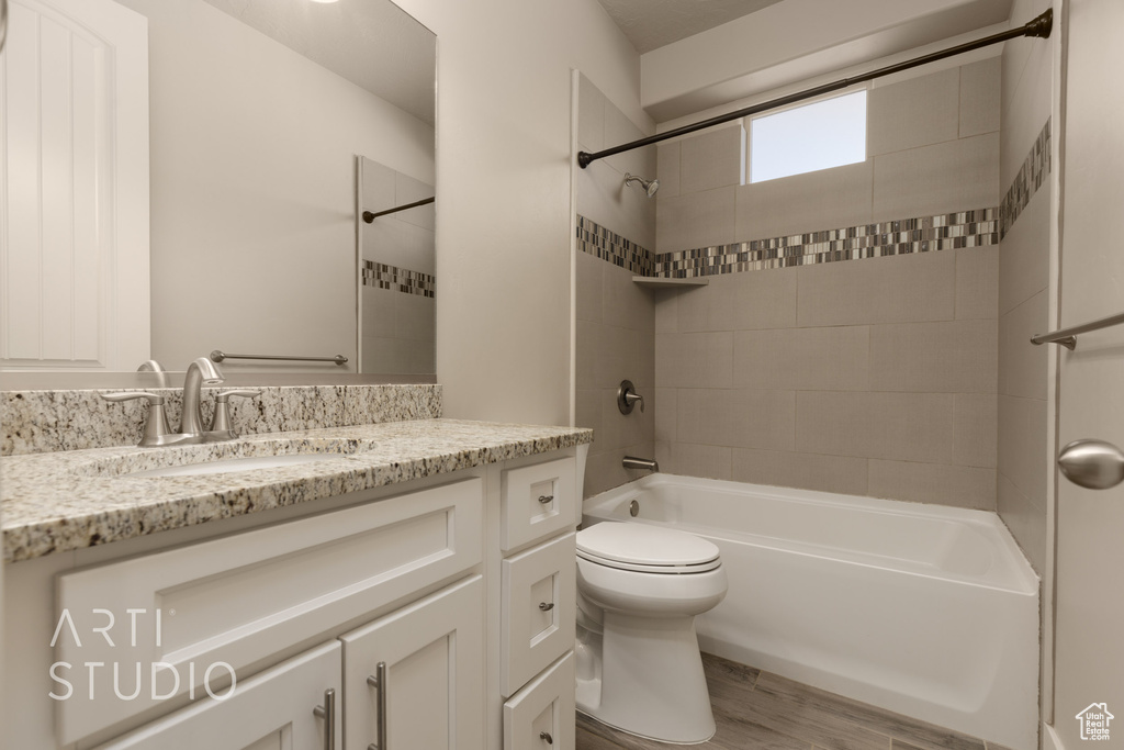 Full bathroom with hardwood / wood-style floors, tiled shower / bath, vanity, and toilet