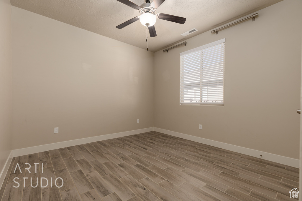 Empty room with a textured ceiling, wood-type flooring, and ceiling fan