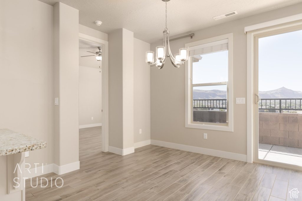 Unfurnished dining area with ceiling fan with notable chandelier, light wood-type flooring, and a mountain view