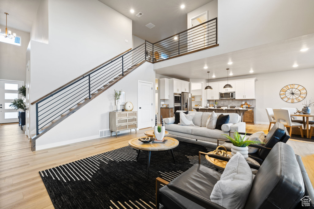 Living room featuring light hardwood / wood-style flooring, a towering ceiling, and an inviting chandelier