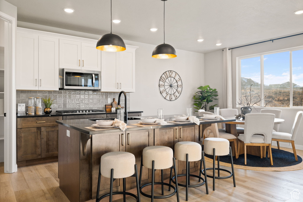 Kitchen featuring white cabinets, a center island with sink, stainless steel appliances, and light wood-type flooring